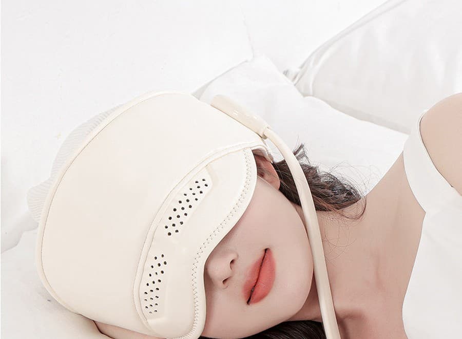 Person lying back in bed wearing the cream Halo head and eye massager, completely relaxed